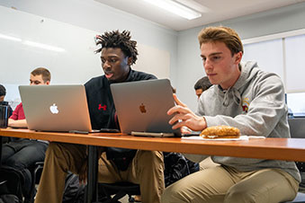 Two students studying on their laptops together. Links to Gifts of Real Estate