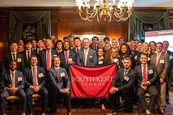 A group of alumni holding a South Kent School banner. Links to Ages 45–65